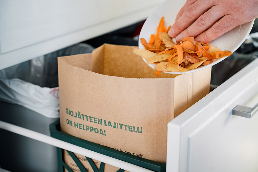 Kuvassa asukas laittaa vihannesten kuoria paperiseen biojätepussiin